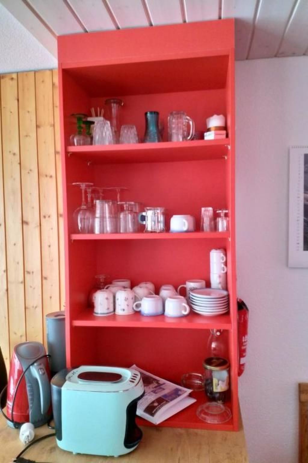 Una estantería roja con diferentes utensilios de cocina.