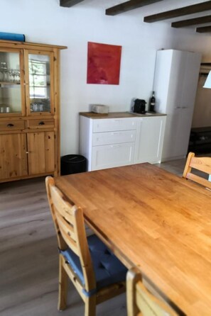 Ett matbord i trä med tillhörande stolar, ett skåp i trä med glasdörrar och ett vitt skåp med lådor.