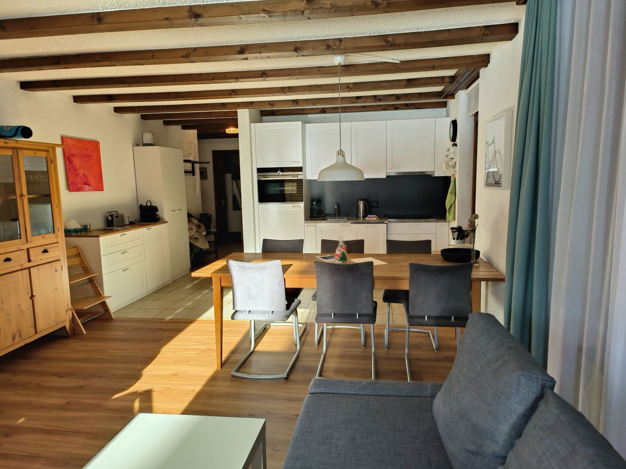 Een moderne keuken met witte kasten, een eethoek met een houten tafel en stoelen, en een bank op de voorgrond.