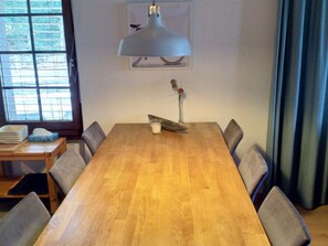 Ein Konferenzraum mit einem langen Holztisch, grauen Stühlen, einer Tischlampe, einer Vase mit Blumen und einem Fenster mit Jalousien.