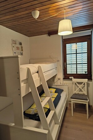 Ein Stockbett mit einer Leiter, einem Schreibtisch und einem Stuhl in einem Zimmer mit Holzboden und einem Fenster mit Jalousien.