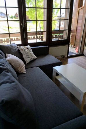 Ein modernes Wohnzimmer mit grauem Sofa, einem weißen Couchtisch und Blick durch große Fenster.
