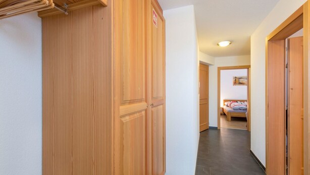 A hallway with wooden doors, a bed in the background, and a tiled floor. - AsterB, (Grächen), by Interhome (Grächen)