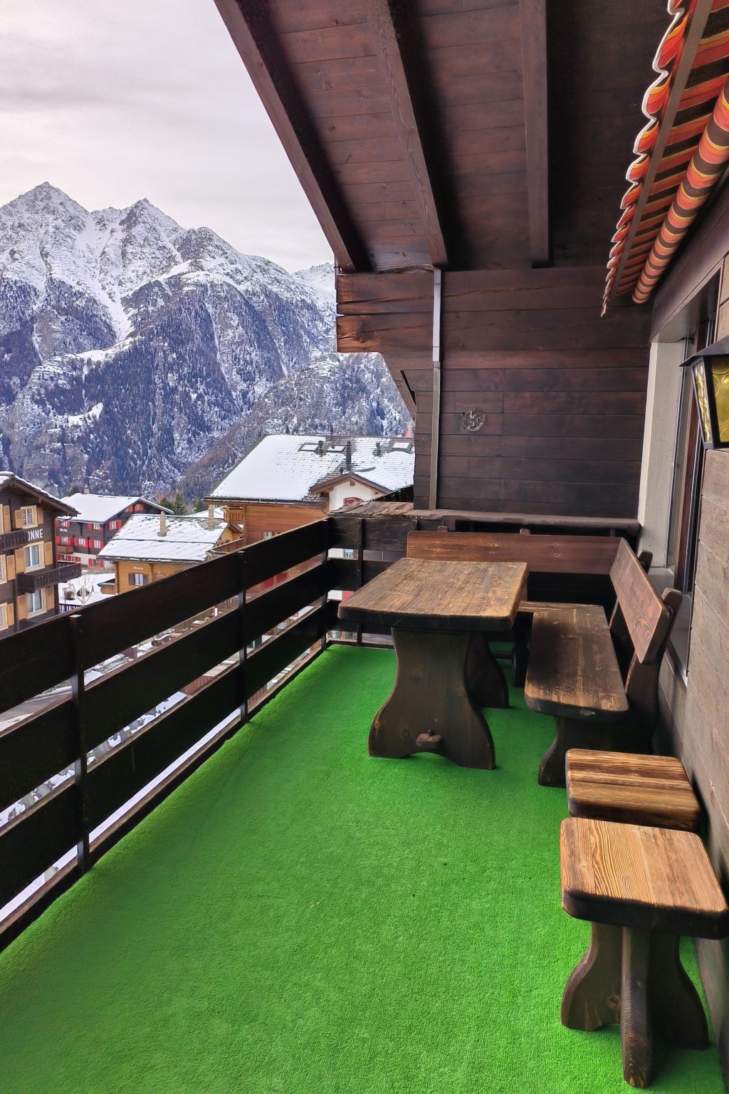 A balcony with a wooden table and benches, a green artificial turf floor, and a mountain view.