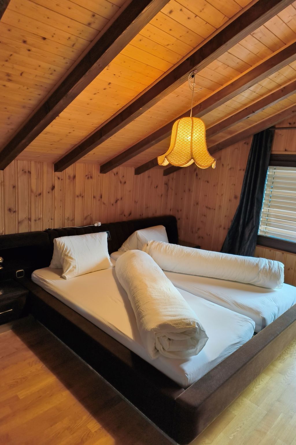 Una habitación con techo de madera, cama con ropa blanca y una lámpara colgante.