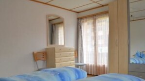 A bedroom with two beds, a dresser, a chair, a mirror, and a window with curtains. - Alpfrieden, (Grächen), 1336 by Interhome (Grächen)