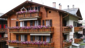 A multi-story wooden building with balconies adorned with flowers, likely a hotel or guesthouse. - Alpfrieden, (Grächen), 1336 by Interhome (Grächen)