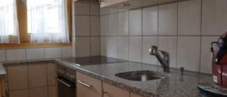 Cozinha com bancada de granito, pia de aço inoxidável e eletrodoméstico vermelho.