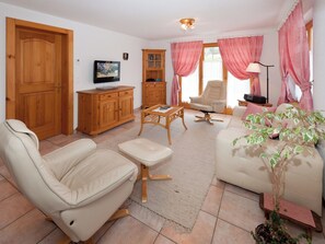 A living room with a sofa, armchair, wooden cabinet, television, and a potted plant. - Stella del Cervino, (Grächen), 2144 by Interhome (Grächen)
