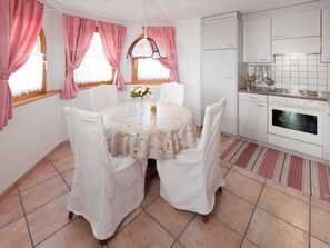 A kitchen with white cabinets, a stove, and a dining area with a table set for two. - Stella del Cervino, (Grächen), 2144 by Interhome (Grächen)