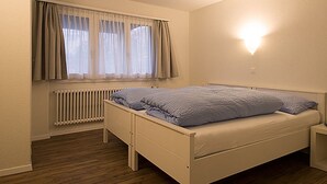 A bedroom with a bed, a window with curtains, a wall-mounted light, and a radiator. - Soldanella, (Grächen), by Interhome (Grächen)