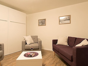A living room with a grey sofa, a brown sofa, a coffee table with a book and a glass of wine, and two framed pictures on the wall. - Ferienwohnungen Soldanella, (Grächen), by Interhome (Grächen)