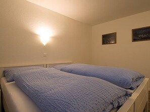 Ein Schlafzimmer mit zwei Betten, einer Wandleuchte und zwei gerahmten Bildern.