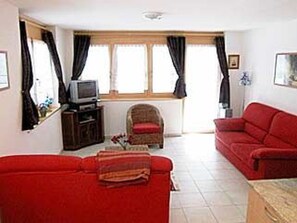 A living room with two red sofas, a television on a wooden stand, and a window with curtains. - Sunstar 10, (Grächen), 1020 by Interhome (Grächen)