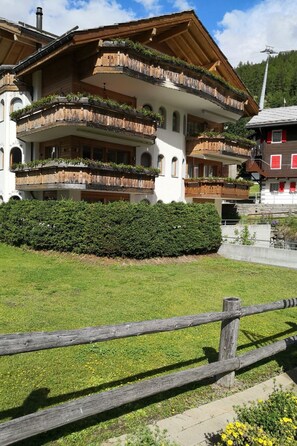 A multi-story building with balconies, a wooden fence, and a well-maintained lawn. - Sunstar 10, (Grächen), 1020 by Interhome (Grächen)
