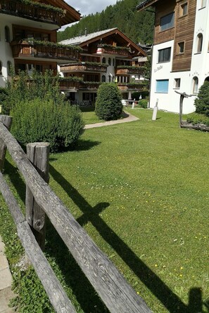 A hotel courtyard with a wooden fence, a well-maintained lawn, and buildings with balconies. - Sunstar 10, (Grächen), 1020 by Interhome (Grächen)