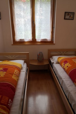 A room with two beds, a small table, and a window with lace curtains. - Sunstar 10, (Grächen), 1020 by Interhome (Grächen)
