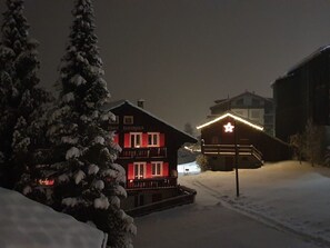 A snow-covered building with a red-lit entrance and a star-shaped sign. - Chalet Heimatglück, (Grächen), 1179 - 1181 by Interhome (Grächen)