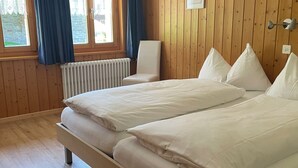 Una cama doble con ropa de cama blanca, un radiador, una silla y paredes de madera.