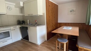 Cocina compacta con lavavajillas, horno y un pequeño comedor con mesa de madera y banco.