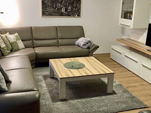 A living room with a sofa, a coffee table, and a TV on a stand. - Chalet Heimatglück, (Grächen), 1179 - 1181 by Interhome (Grächen)