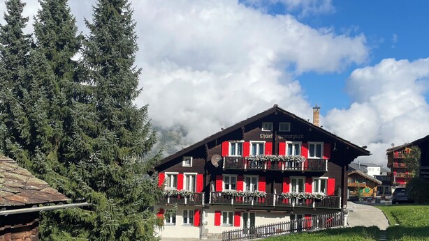 Un edificio de estilo chalé con contraventanas rojas, balcones con jardineras y cielo despejado.