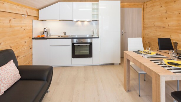 A compact kitchen with white cabinets, a built-in oven, and a dining area with a wooden table and chairs. - Ferienwohnungen Miranda, (Grächen), by Interhome (Grächen)