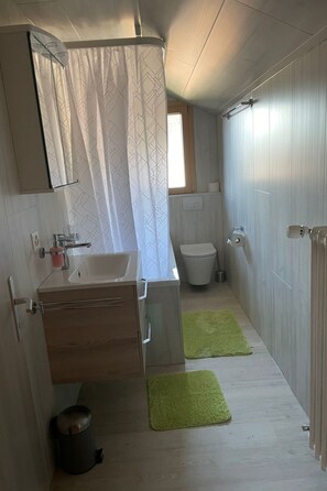 A compact bathroom with a sink, toilet, and shower curtain. - Ferienwohnungen Miranda, (Grächen), by Interhome (Grächen)