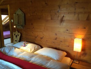 A wooden cabin room with two beds, a small wooden chest, and a wall-mounted lamp. - Ferienwohnungen Chalet Safran, (Grächen), 1063 & 1594 by Interhome (Grächen)