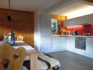A modern kitchen with white cabinetry, a wooden dining table, and a fur throw on the chair. - Ferienwohnungen Chalet Safran, (Grächen), 1063 & 1594 by Interhome (Grächen)