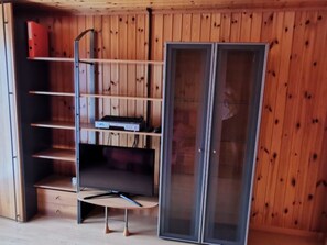 A room with a wooden wall, a metal shelf unit, and a sliding glass door. - Ferienwohnungen Bergtreu, (Grächen), by Interhome (Grächen)