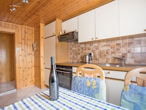 A kitchen with wooden cabinets, a tiled backsplash, a stove, and a table with a checkered tablecloth. - Ferienwohnungen Bergtreu, (Grächen), by Interhome (Grächen)