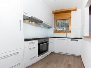 A compact kitchen with white cabinets, a black countertop, a built-in oven, and a window with a view of trees. - Metropol B28, (Grächen), by Interhome (Grächen)