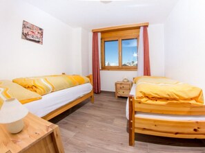 A bedroom with two wooden beds, a nightstand, a lamp, and a window with curtains. - Metropol B28, (Grächen), by Interhome (Grächen)