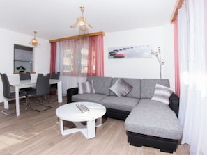 A modern living room with a grey sectional sofa, a white coffee table, and a dining area with a white table and chairs. - Metropol B28, (Grächen), by Interhome (Grächen)