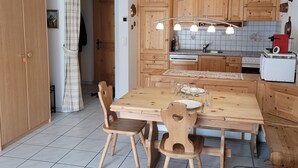 A kitchen with wooden cabinets, a dining table with chairs, and a red appliance. - Metropol B19, (Grächen), 1079 by Interhome (Grächen)