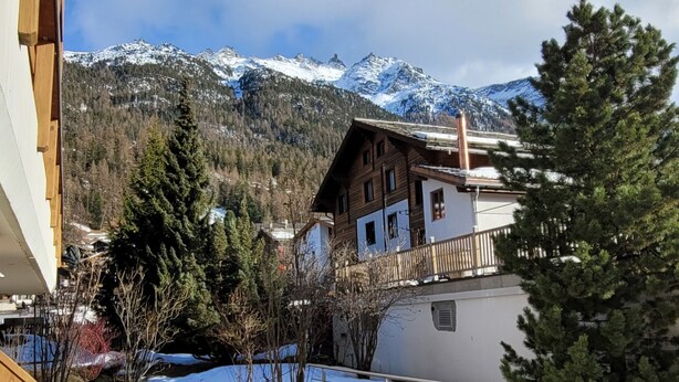 A mountain cabin with a wooden exterior, a balcony, and a view of snow-capped mountains. - Metropol B19, (Grächen), 1079 by Interhome (Grächen)