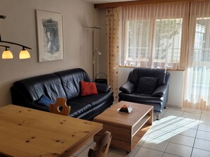 Ett vardagsrum med en svart lädersoffa, ett soffbord i trä och en svart fåtölj.