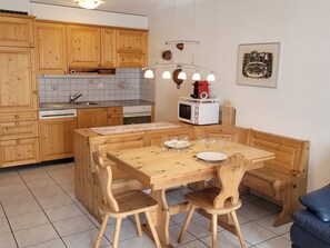 Ett kompakt kök med träskåp, en mikrovågsugn och en matplats med ett träbord och stolar.