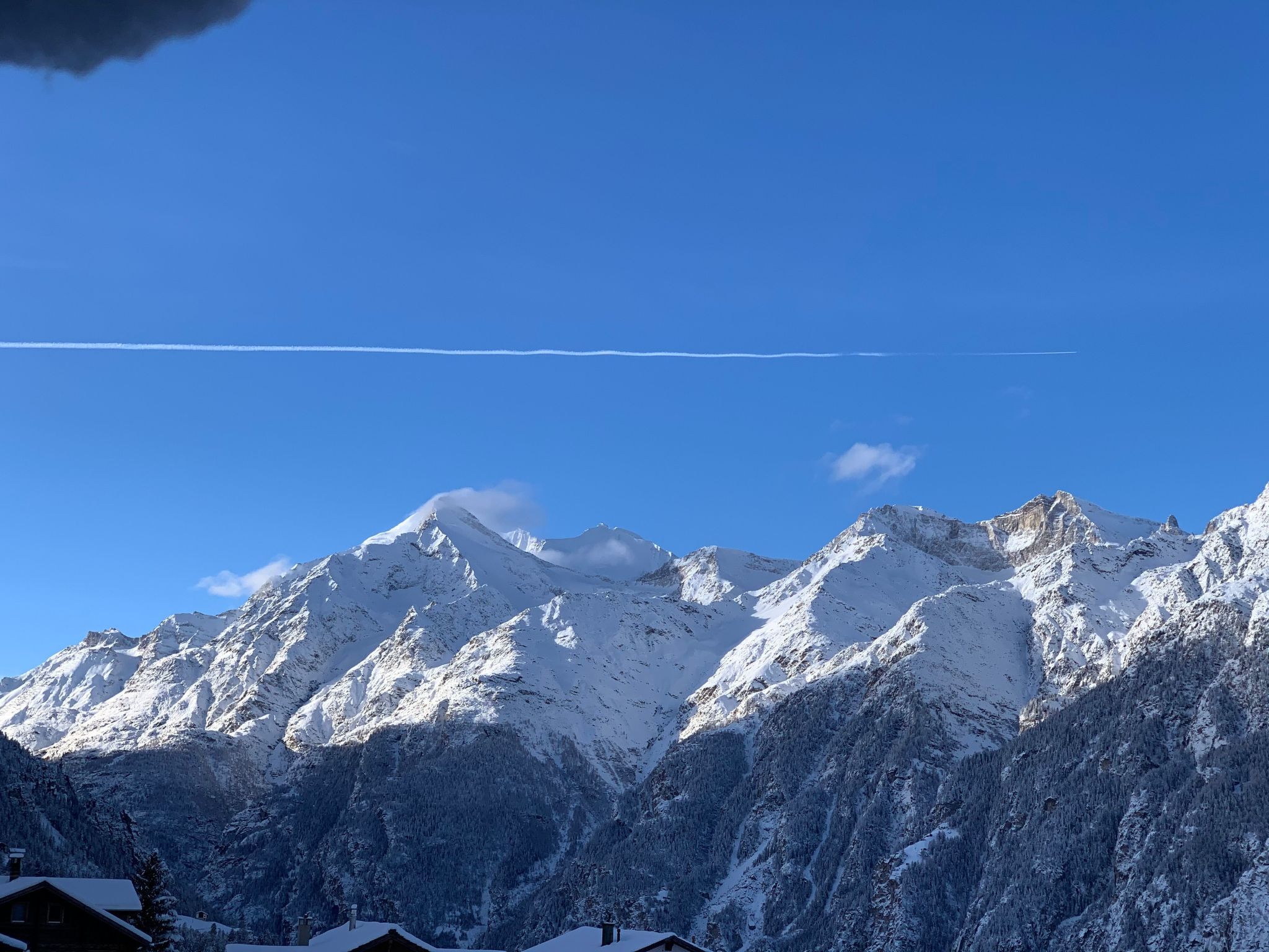 A snow-covered mountain range with a clear sky and a visible contrail.
