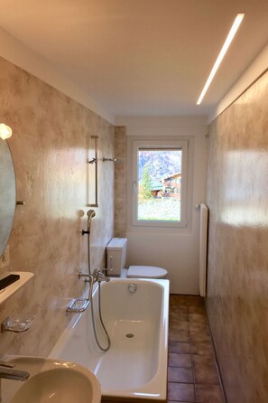 Een badkamer met een bad, toilet en een raam met uitzicht op gebouwen.