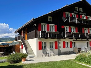 A two-story building with a balcony, a staircase, and a view of the mountains in the background. - Chalet Heimatglück, (Grächen), 1179 - 1181 by Interhome (Grächen)