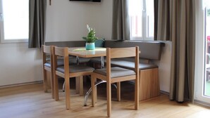 A dining area with a wooden table and chairs, a potted plant, a television mounted on the wall, and a cross on the wall. - Chalet Heimatglück, (Grächen), 1179 - 1181 by Interhome (Grächen)