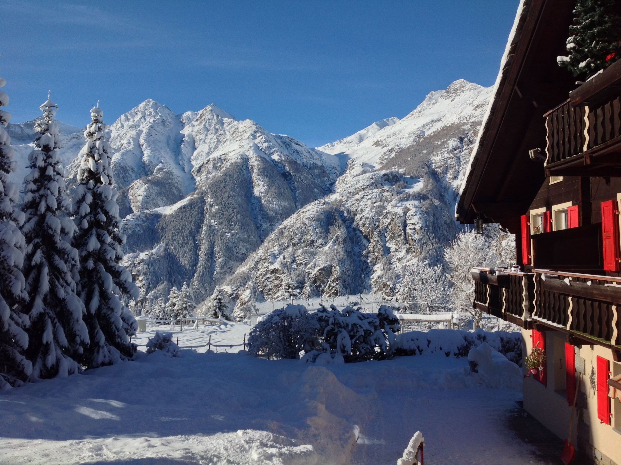 Schneebedeckte Berglandschaft mit einem Holzhaus und roten Fensterläden.