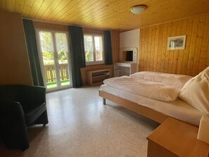 Een kamer met een bed, een bureau en een stoel. Er is een raam met gordijnen en uitzicht op groen.