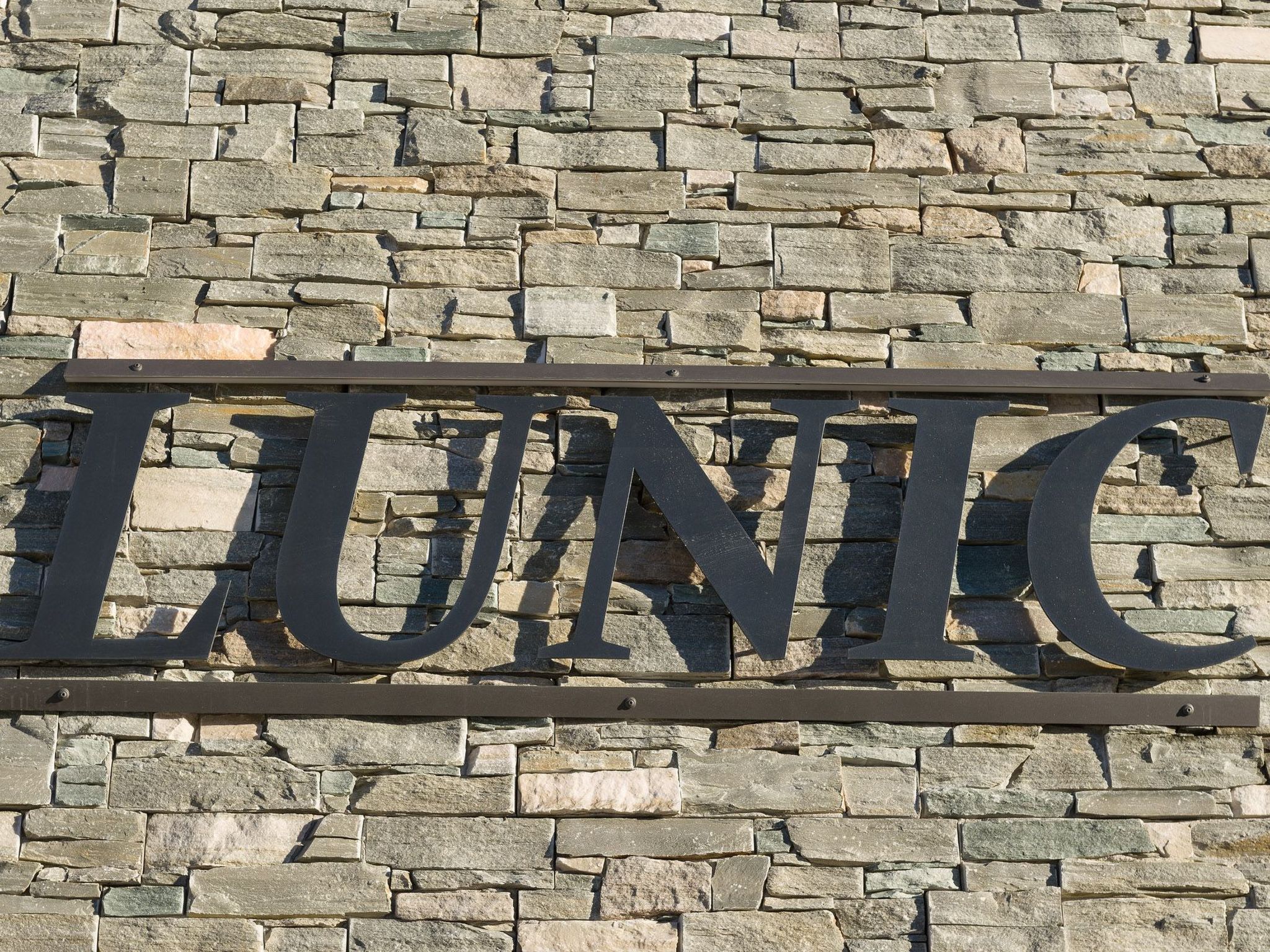 A stone wall with a metal sign spelling 'LUNIC'.
