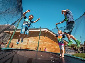 A trampoline with netted safety barriers, wooden beams, and a clear blue sky.