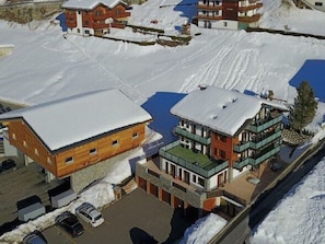 A snow-covered building complex with multiple structures, including a large wooden building and several modern buildings with balconies.