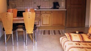 Ein kompakter Wohnraum mit einer Küchenzeile, einem Essbereich mit Stühlen, einer Couch und einem Streifenmuster-Teppich.