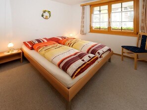 A bedroom with a bed, a nightstand, a chair, a window with curtains, and a wall decoration. - Nr. 20 Sierra Vista, (3925 Grächen), 5001 by Interhome (Grächen)